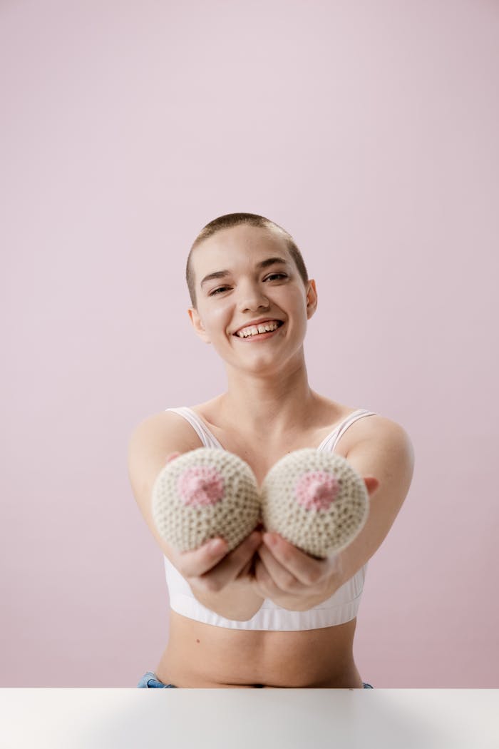 Cheerful young woman with short hair holding knitted breasts, promoting breast cancer awareness.