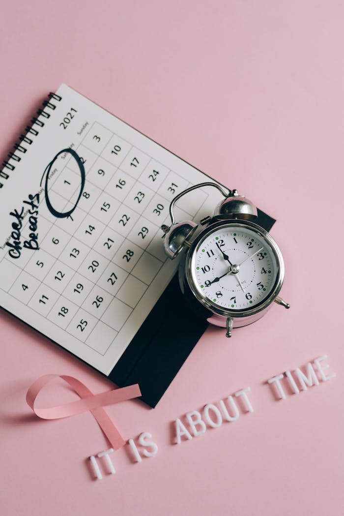 Elegant flat lay promoting breast cancer awareness with pink ribbon, calendar, and alarm clock.